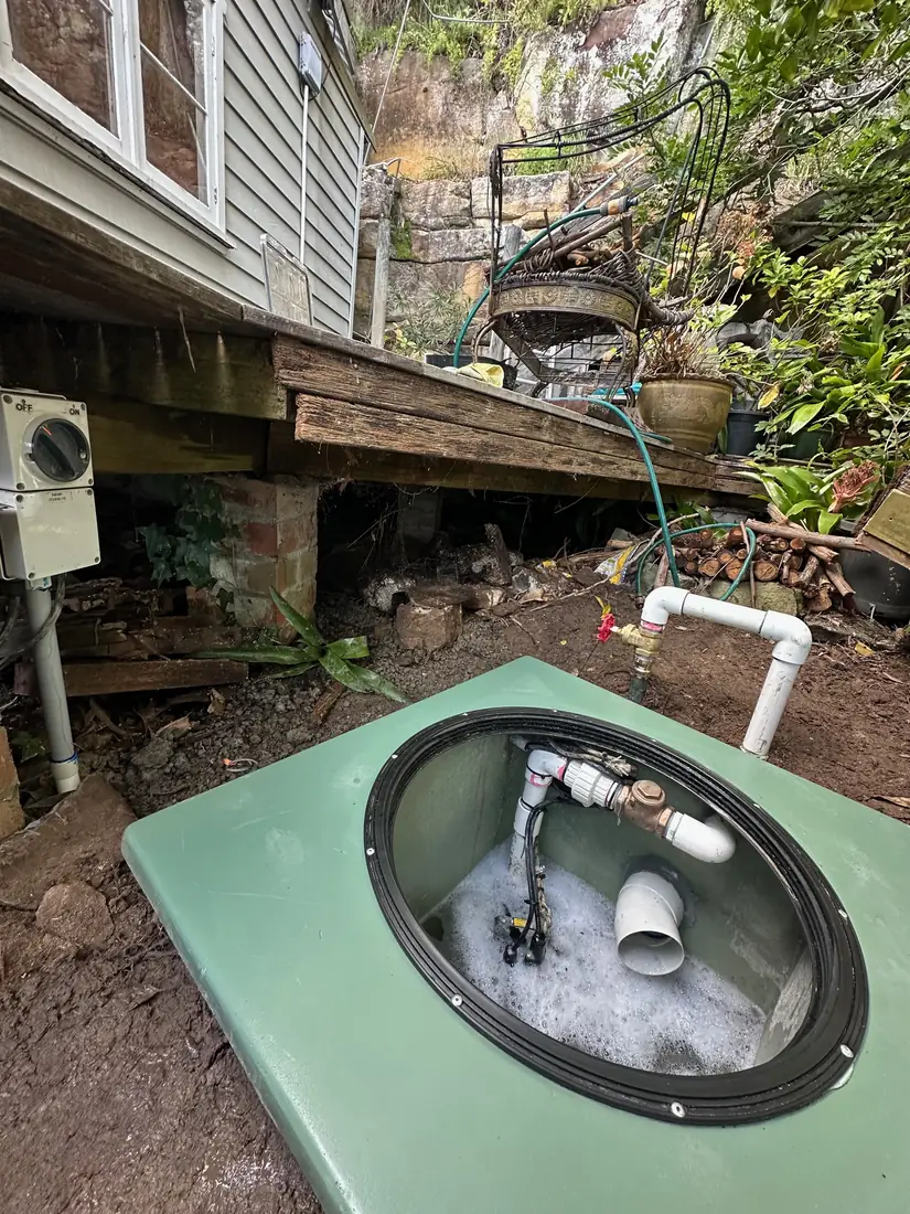 The finished Illawong pit with the manhole open, showing the new discharge pipework, check valve and switch on the post behind
