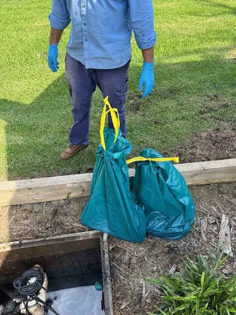 Service technician with two waste bags of debris removed from pump pit, ready for offsite disposal