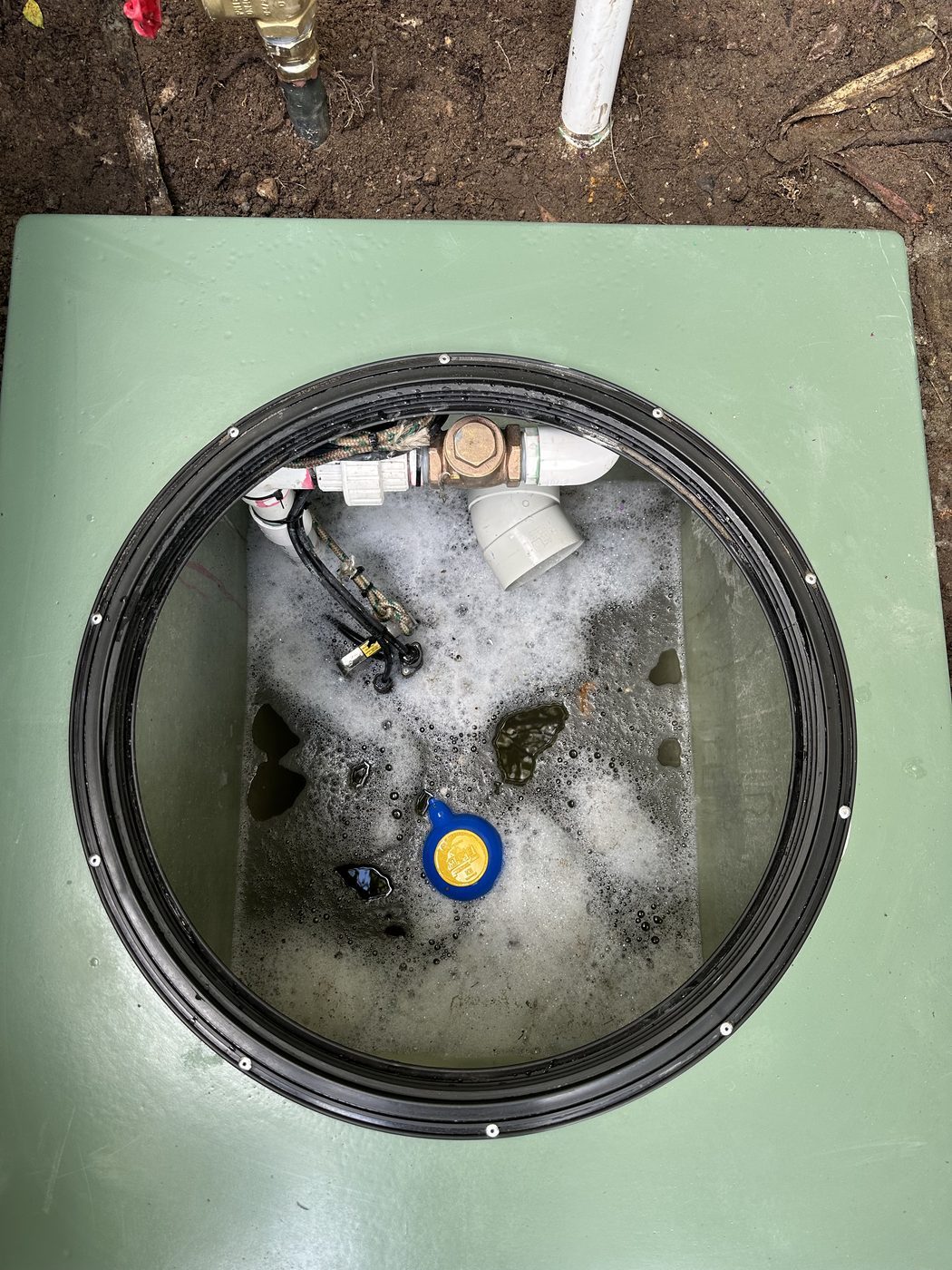 Inside a pump pit showing the brass non-return valve and union on the horizontal run, the discharge elbow turning up and out, and a float hanging alongside