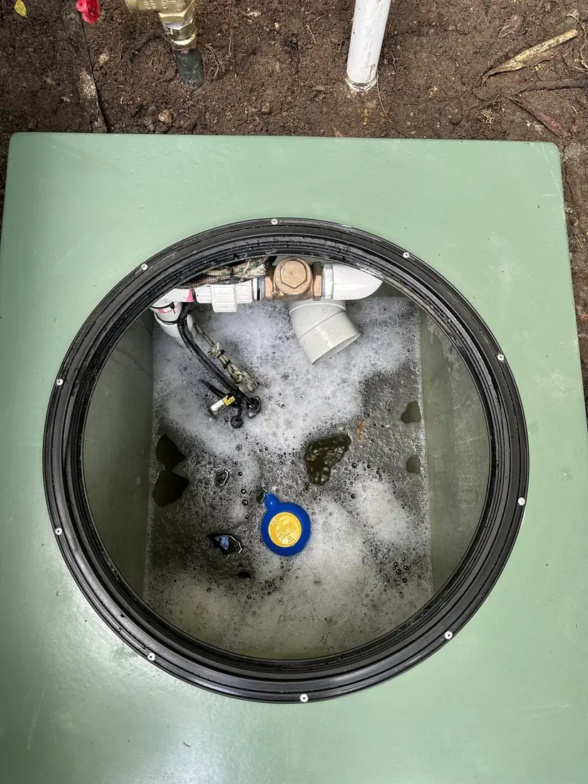 Inside a pump pit showing the brass non-return valve and union on the horizontal run, the discharge elbow turning up and out, and a float hanging alongside