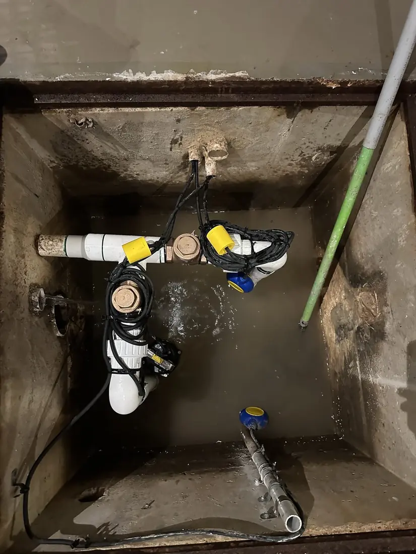A two-pump pit with two pumps, brass non-return valves on the horizontal runs, and the float and pump cabling coiled and tied back clear of the water