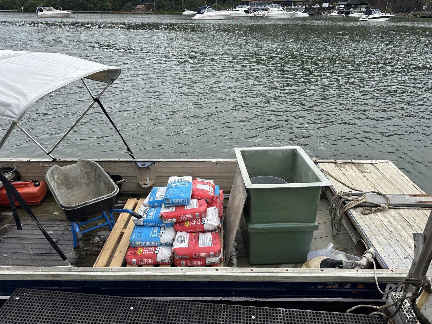 New fibreglass pump pit, bags of concrete and a wheelbarrow loaded on a barge for delivery to a waterfront Sydney property