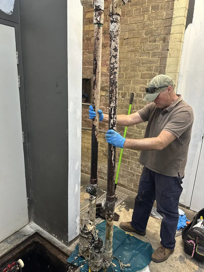 Stuart servicing a Sydney grease trap pump pit, dual rising mains caked in hardened fat from kitchen FOG output